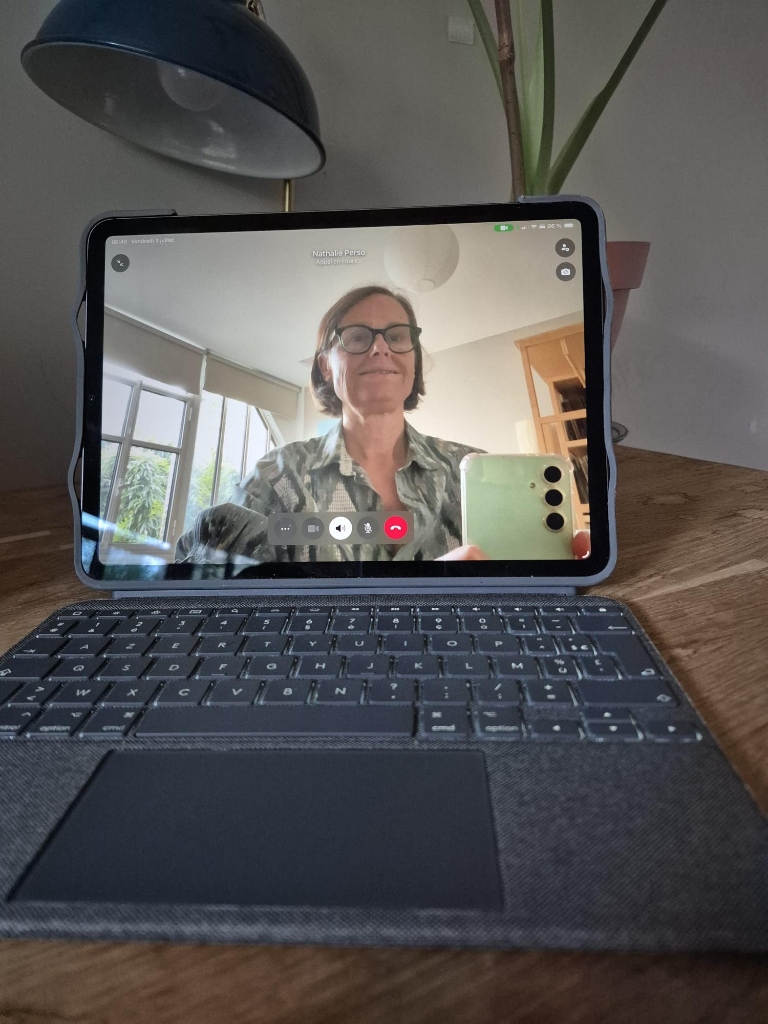 Une tablette affichant une visioconférence avec Nathalie Suzanne sur un bureau en bois